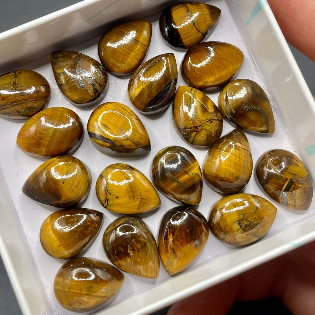 Box of teardrop-shaped tiger's eye stones held by a hand.