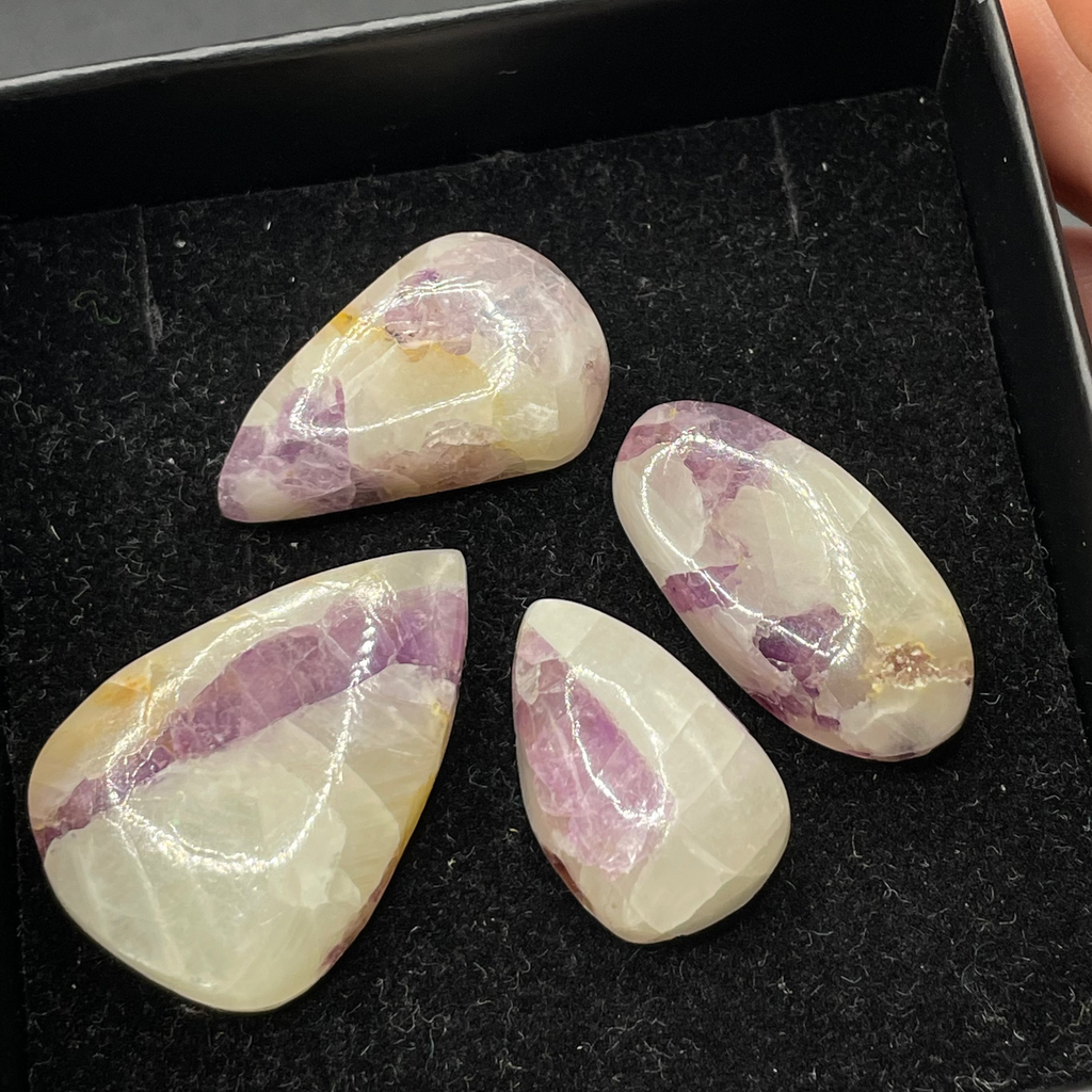 Five teardrop-shaped purple and white stones on a black tray.