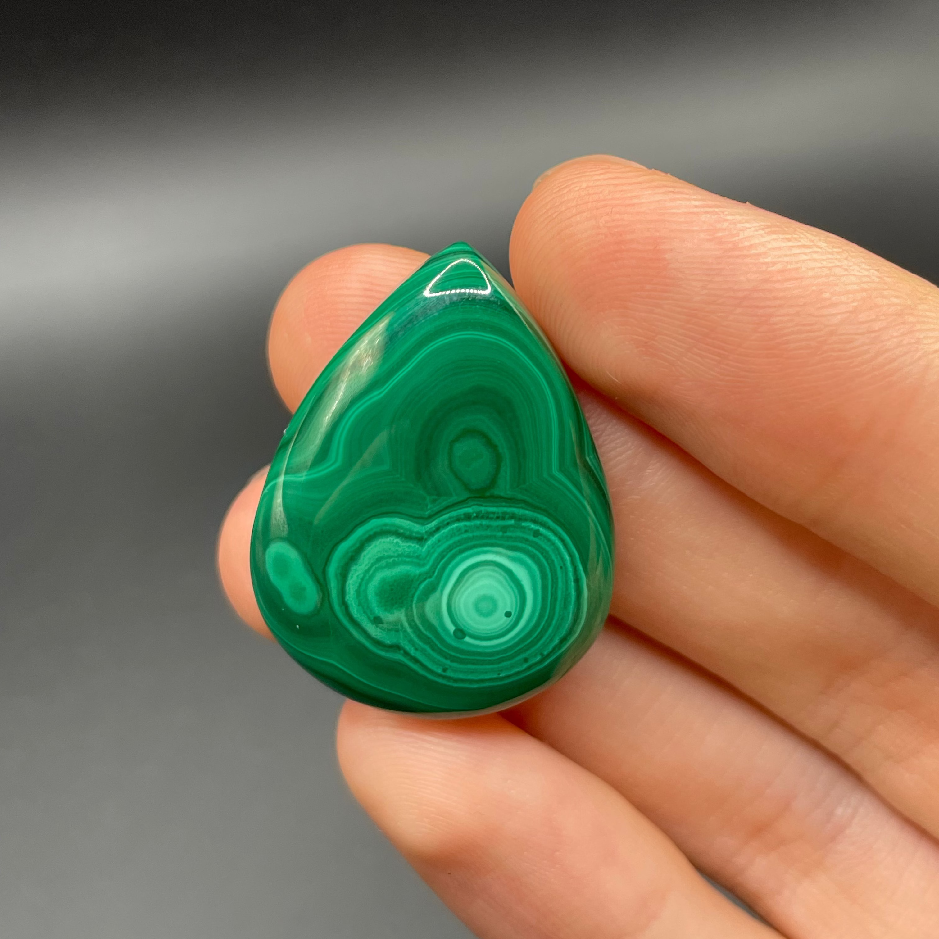 Hand holding a green malachite cabochon against a dark background