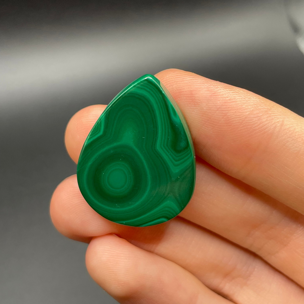Green malachite stone held in a hand against a dark background
