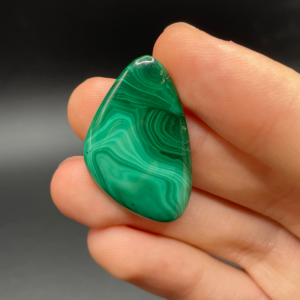 Hand holding a green malachite stone against a dark background