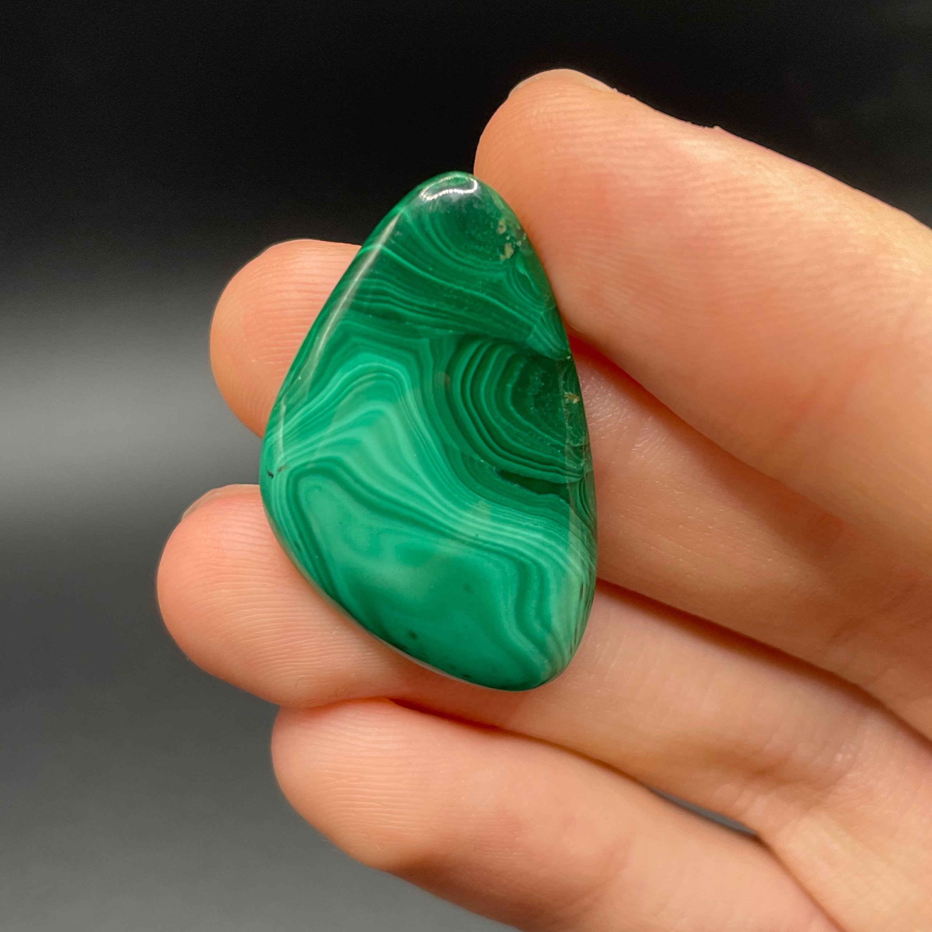 Hand holding a green malachite stone against a dark background