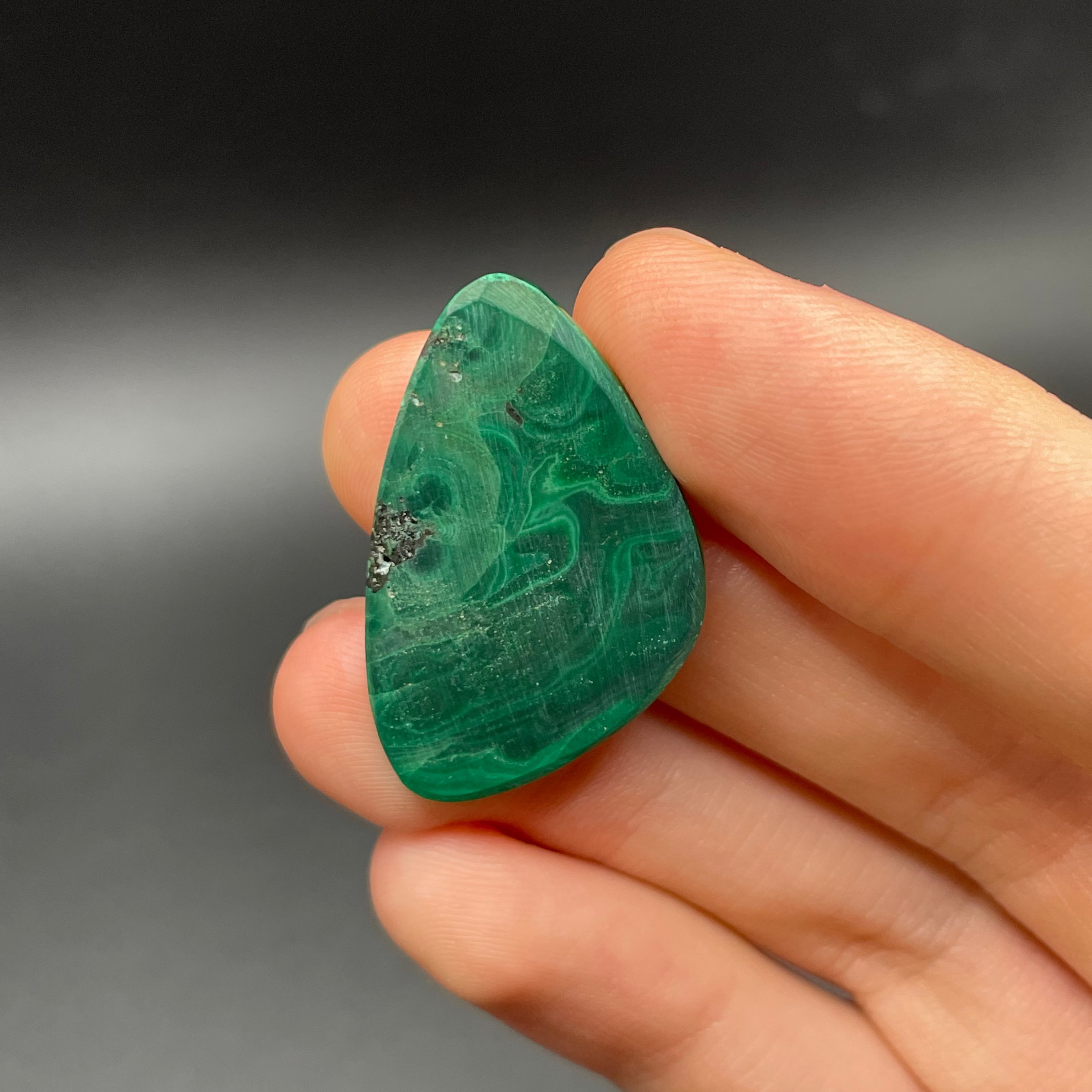 Hand holding a green malachite stone against a dark background