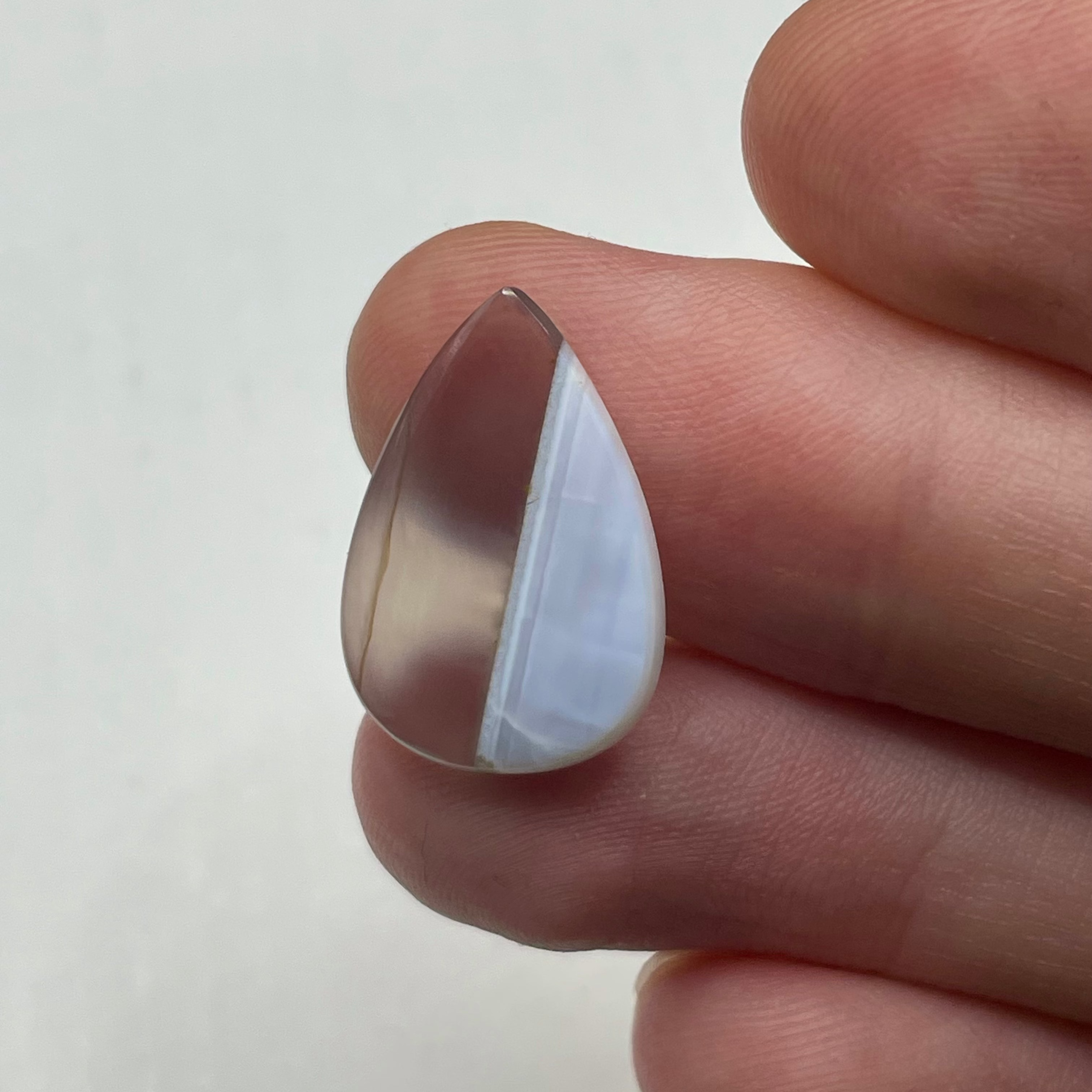 Teardrop-shaped crystal held between fingers on a white background