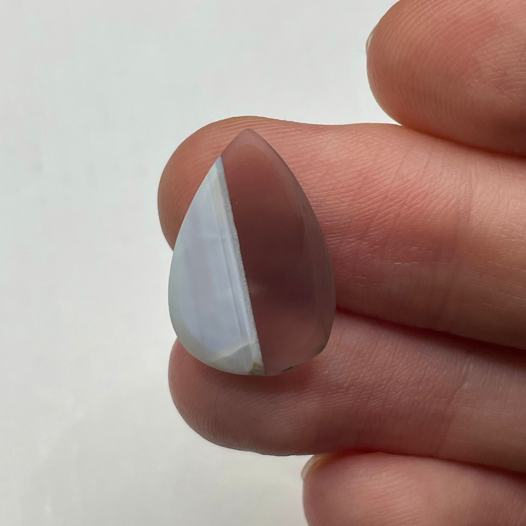 Teardrop-shaped crystal held between fingers on a white background