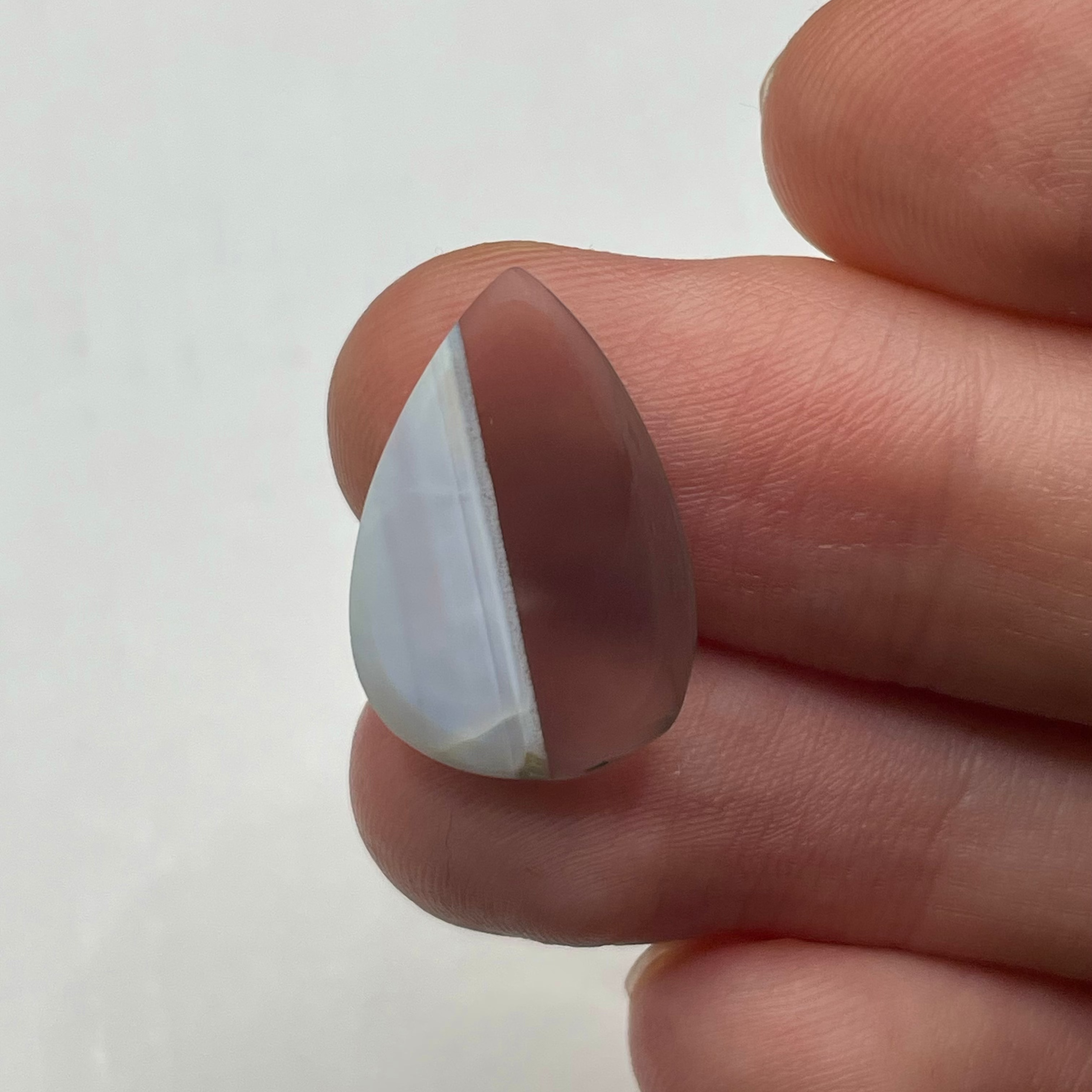 Teardrop-shaped crystal held between fingers on a white background